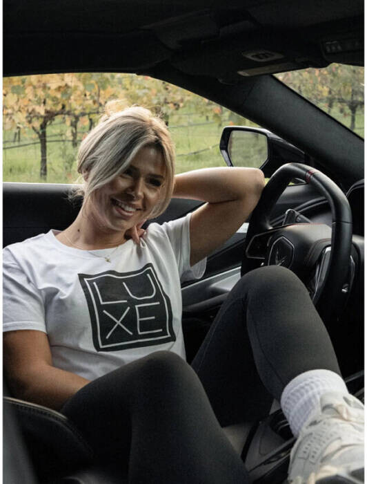 Woman-wearing-White-T-Black-Print-of-Logo-in-Car From Sacramento to the National Stage: Luxe Co. is Rewriting the Narrative of Accessible Luxury  